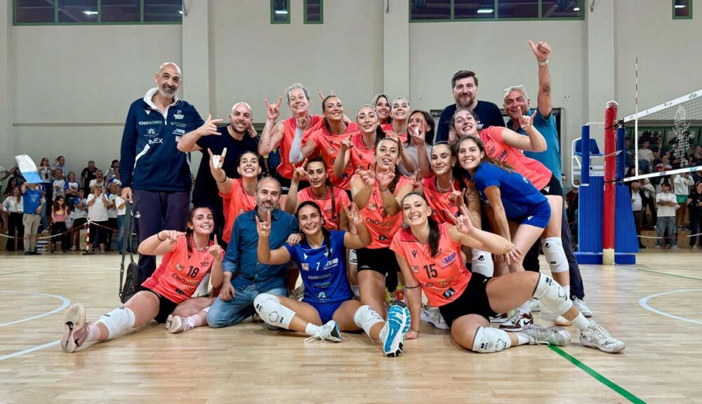 La squadra dell'EnoDoro Marsala Volley festeggia in campo la vittoria a Riccione e l’accesso alla finale per la promozione in Serie A2, sorrisi e mani alzate in segno di vittoria.