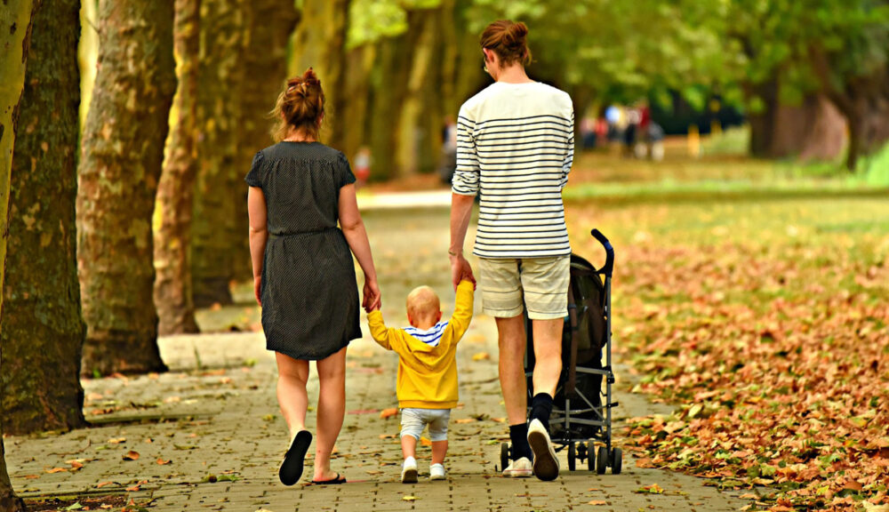 Famiglia che passeggia in un viale alberato: madre, padre e bambino mano nella mano, simbolo dell'amore genitoriale.