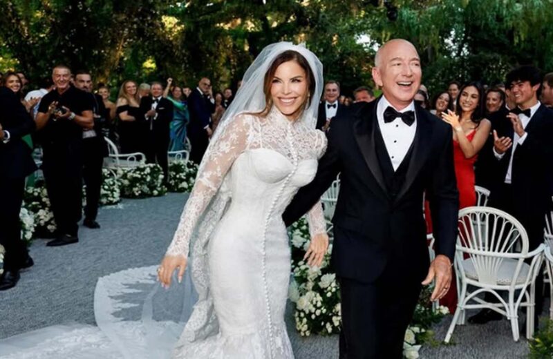 Jeff Bezos e Lauren Sanchez sorridenti dopo il matrimonio, camminano mano nella mano tra gli ospiti festanti in un elegante giardino addobbato con fiori bianchi.