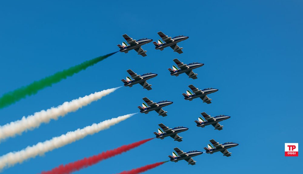 Frecce Tricolori in volo con scie verde, bianca e rossa sul cielo azzurro