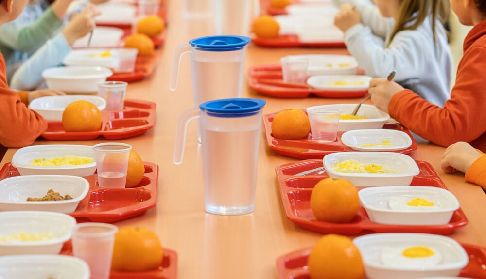 Bambini alla mensa scolastica con vassoi rossi, frutta e pasti