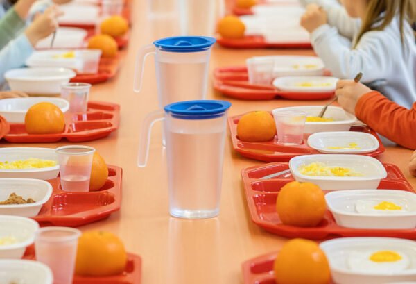 Bambini alla mensa scolastica con vassoi rossi, frutta e pasti