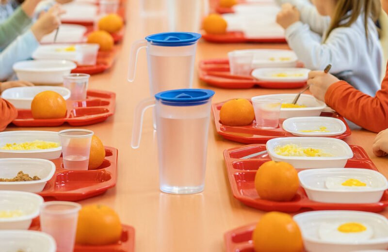 Bambini alla mensa scolastica con vassoi rossi, frutta e pasti